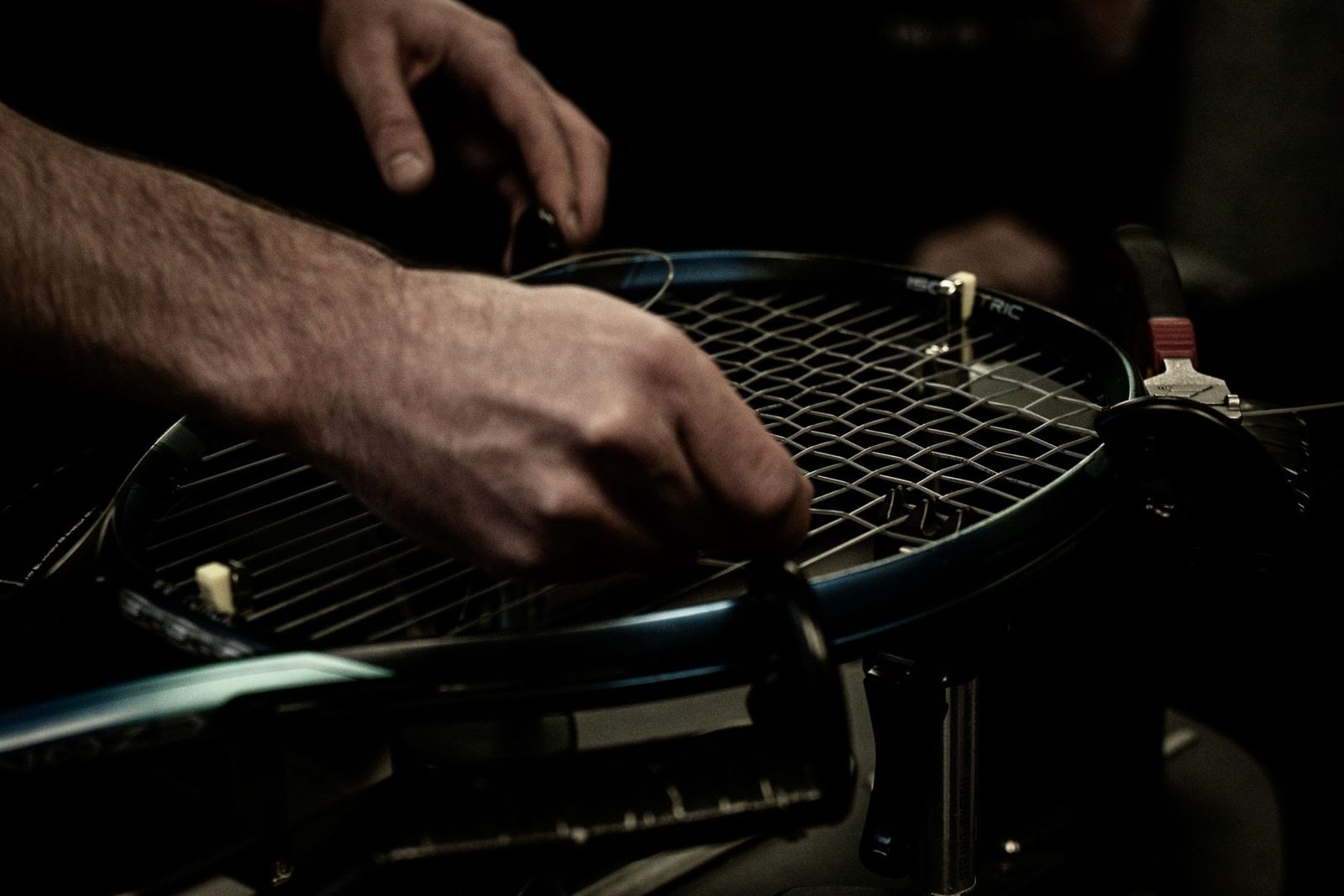 Hands restringing a tennis racket on a stringing machine